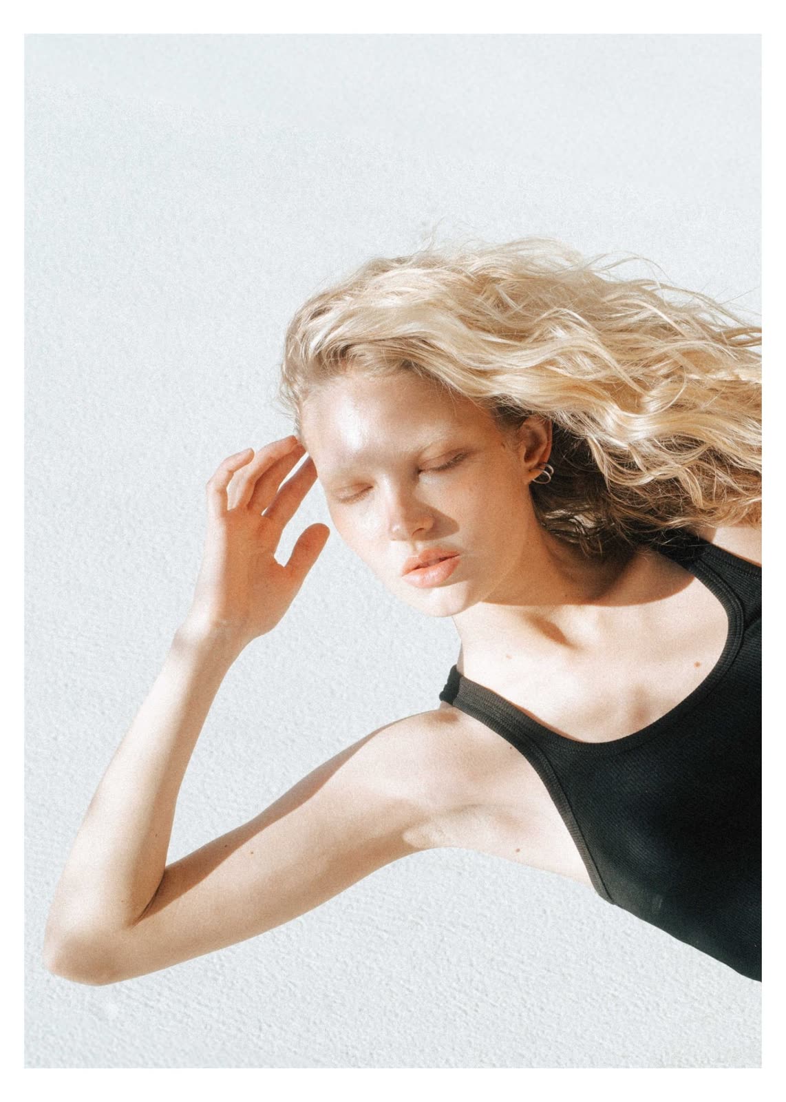 Blonde model in a black top with a hand to her head, pale studio — NIKA, by Kenneth Kemp