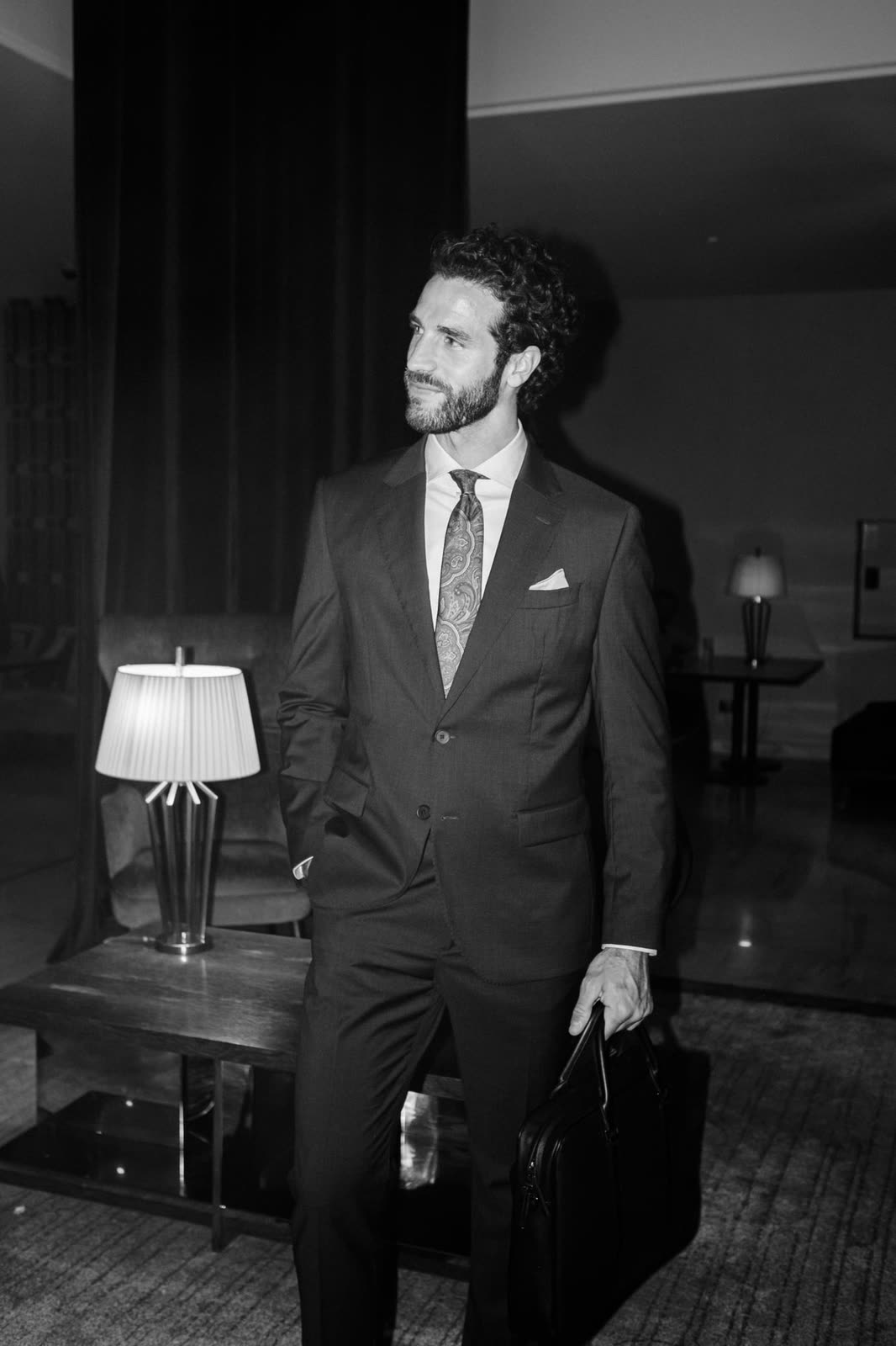 Black and white frame of a man in a suit with a bag in a hotel interior — TIVOLI, by Kenneth Kemp