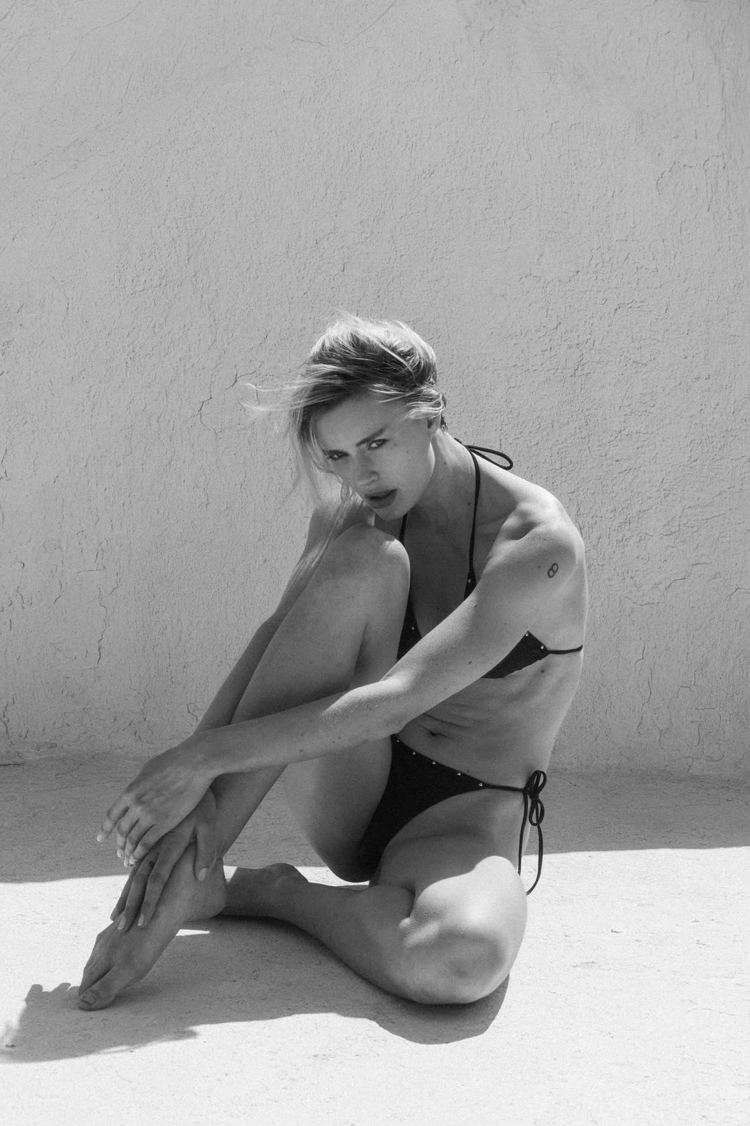Black and white studio frame of a model crouching on a pale floor — GLORIA, by Kenneth Kemp